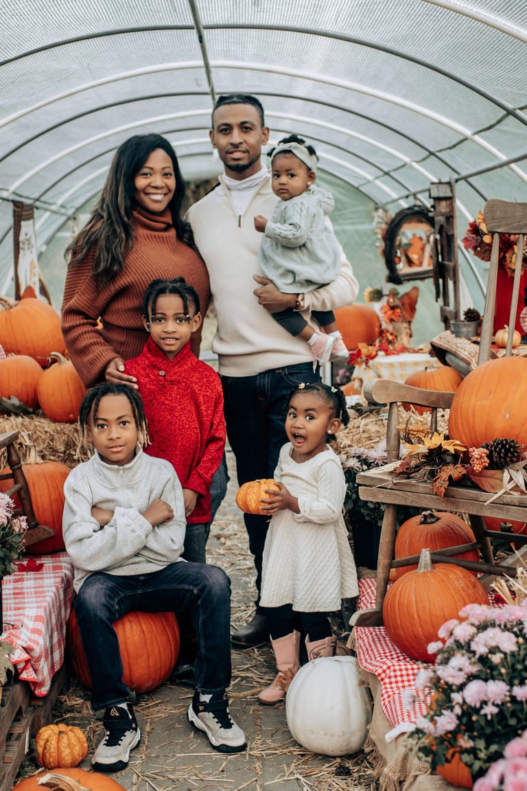 Family of six posing in a greenhouse surrounded by pumpkins, hay bales, and fall decorations